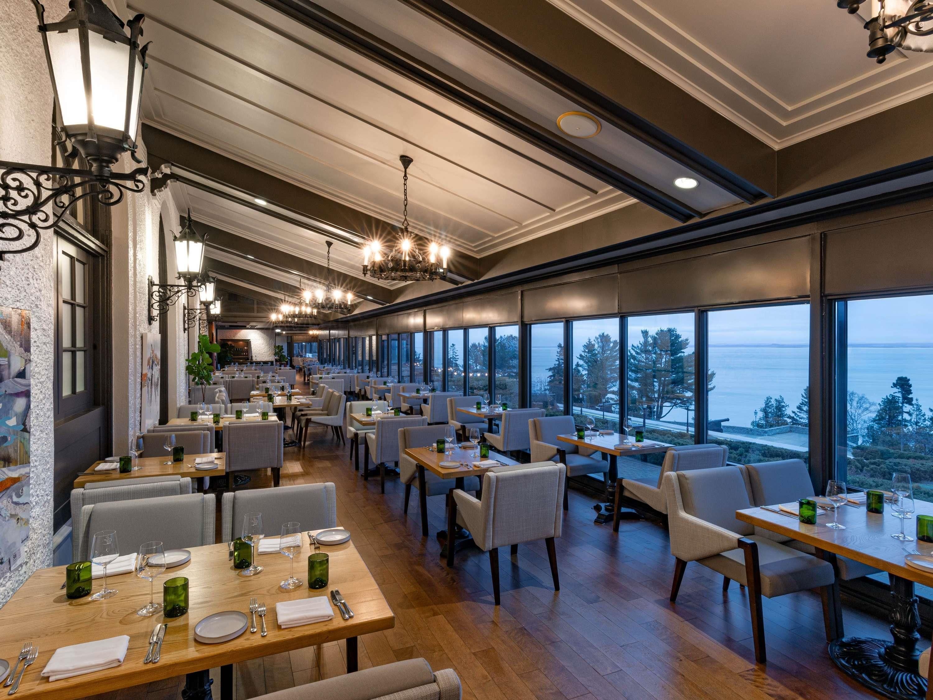 A restaurant with multiple tables, chairs, and a view of the sea.