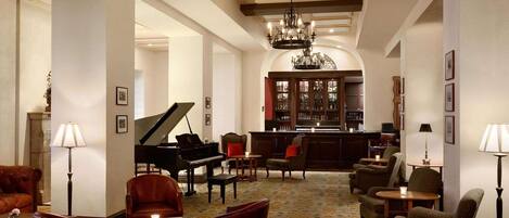 Un'ampia hall con un pianoforte a coda, comodi posti a sedere, un'area bar e un lampadario.