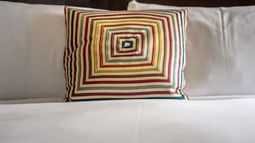 A bed with a white mattress and a multicolored, striped pillow.