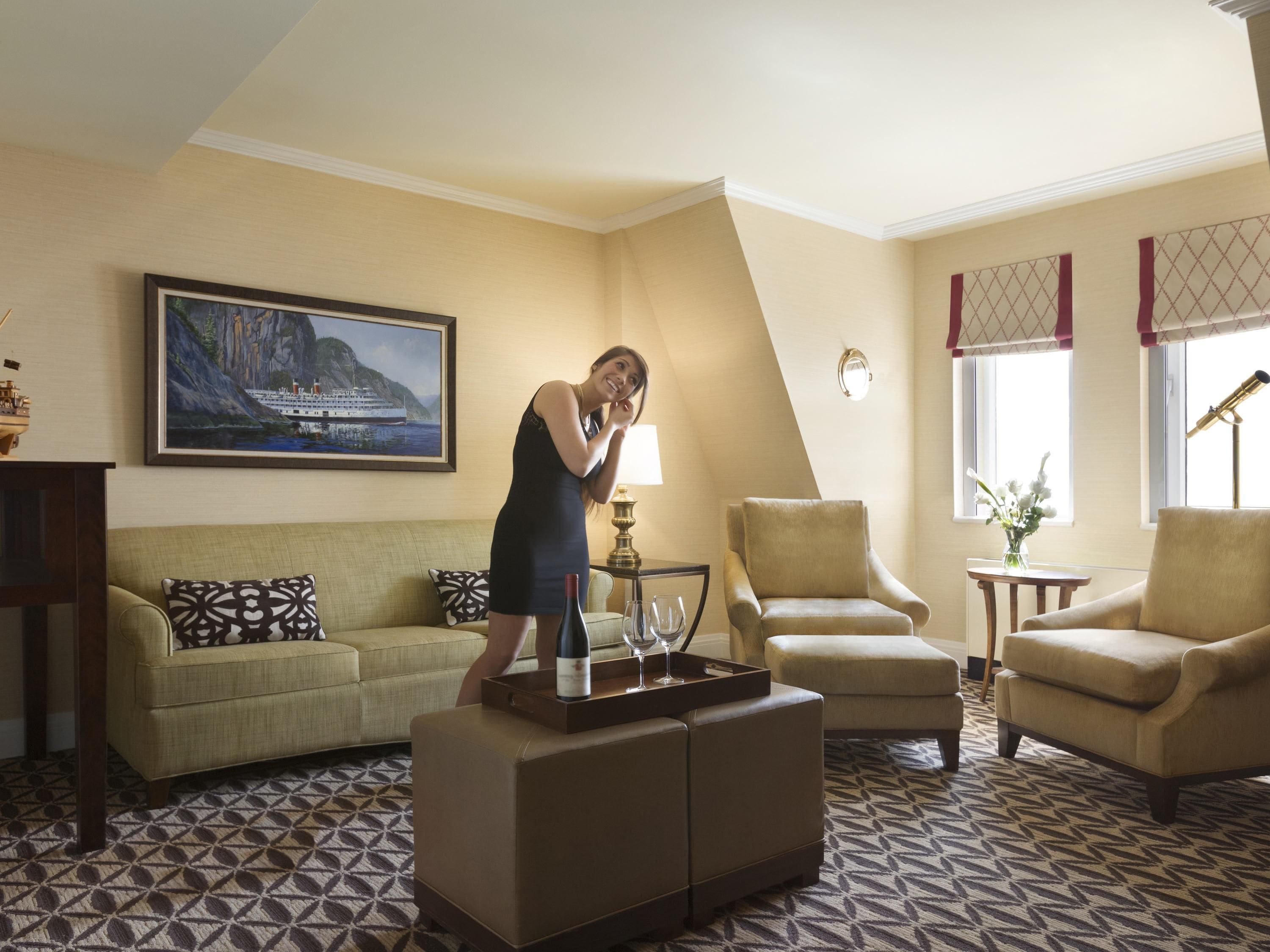 A well-lit living room with a sofa, armchairs, a coffee table, and a painting of a coastal scene.