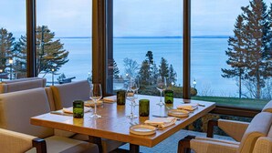 A dining table with chairs, set for a meal, overlooking a body of water and trees. - Fairmont Le Manoir Richelieu (La Malbaie)