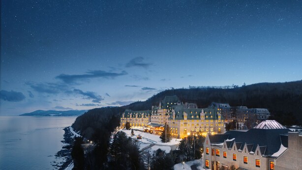 A large, historic hotel with multiple wings, situated by a body of water and surrounded by snow-covered trees. - Fairmont Le Manoir Richelieu (La Malbaie)