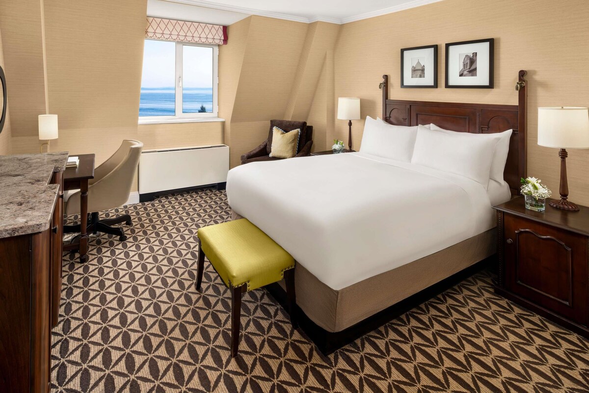 A hotel room with a large bed, a desk, a chair, and a window with a view.