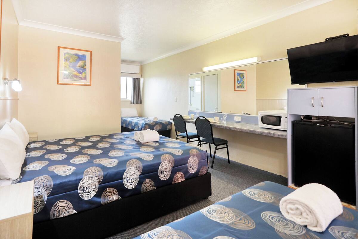 A hotel room with a bed, a desk, a chair, a microwave, and a refrigerator.