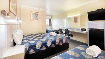 Habitación de hotel con una cama, un escritorio, una silla, un microondas y un refrigerador.