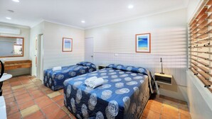 A hotel room with two beds, a desk, a chair, a mirror, a window with blinds, and a wall-mounted shelf.