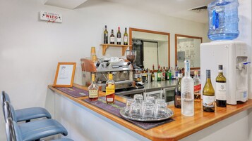 Una zona de bar con una máquina de café, diversas botellas de alcohol y un dispensador de agua.