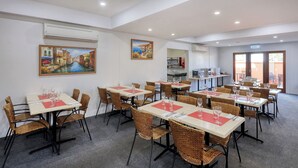 A dining area with tables and chairs, air conditioning units, and artwork on the walls.