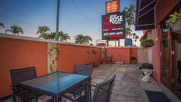 A hotel patio with outdoor seating, a large digital signboard, and a view of palm trees.