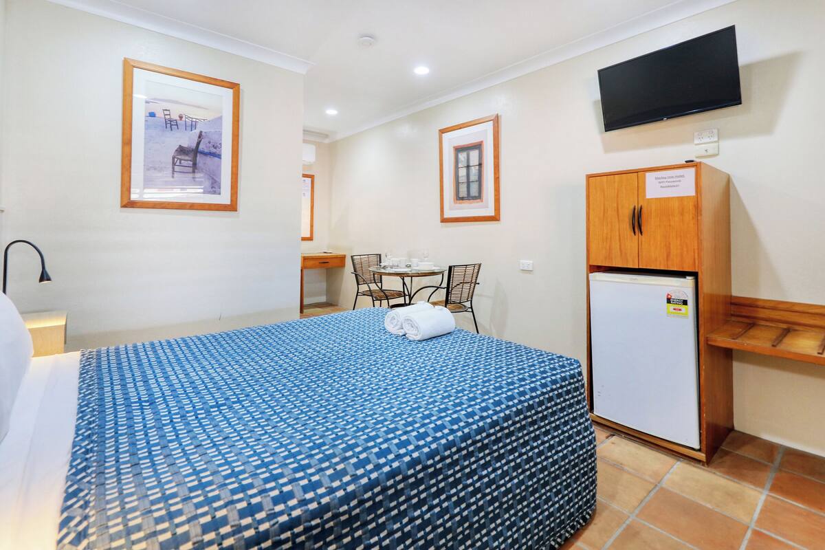 A hotel room with a bed, a desk, a chair, a television, and a refrigerator.