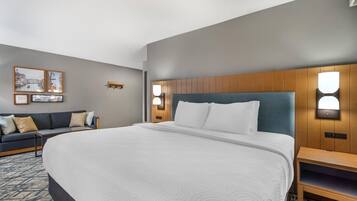 Habitación de hotel con una cama grande, cabecero de madera, dos mesitas de noche, un sofá e iluminación en la pared.