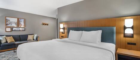 A hotel room with a large bed, a wooden headboard, two bedside tables, a sofa, and wall-mounted lights.