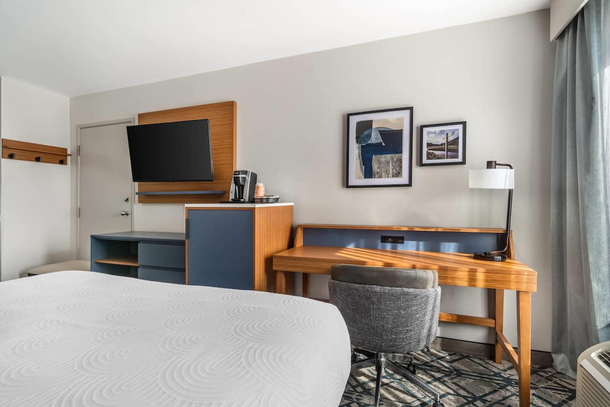 Une chambre d’hôtel avec un grand lit, un bureau avec une chaise, une télévision et deux tableaux encadrés au mur.
