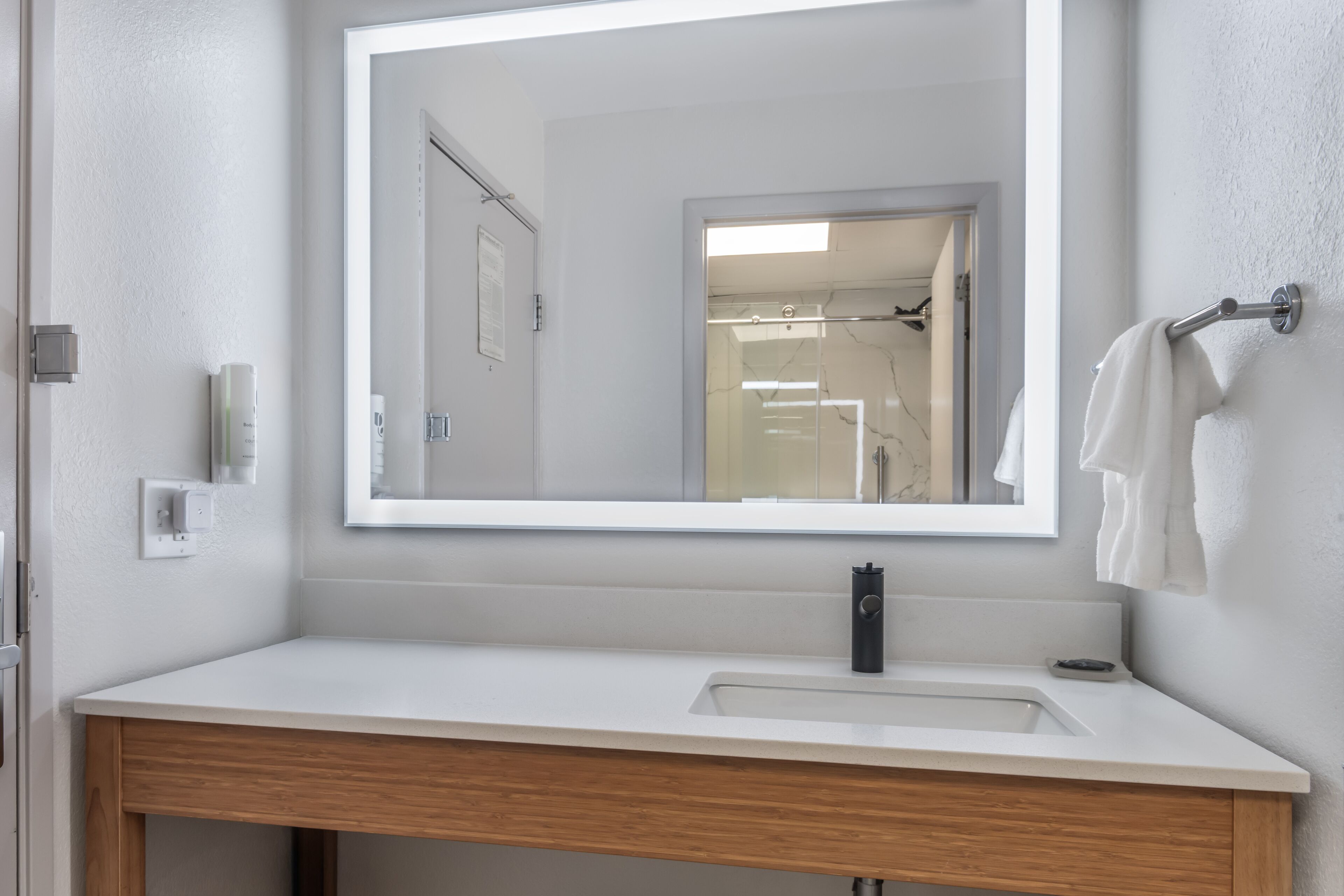 A bathroom with a large mirror, a sink, and a towel rack.