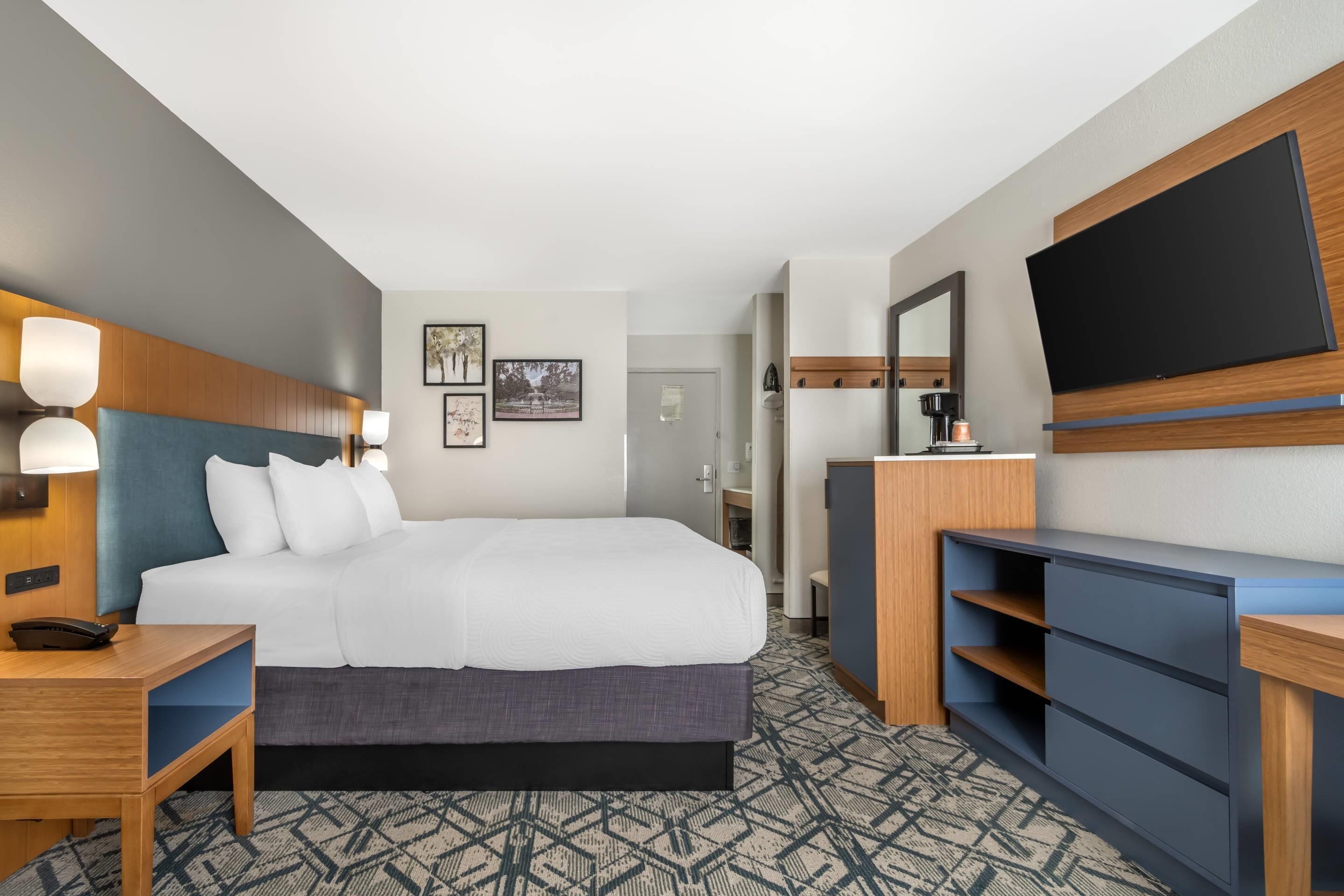 A hotel room with a large bed, bedside tables, a desk, a dresser, a flat-screen TV, and a mirror.