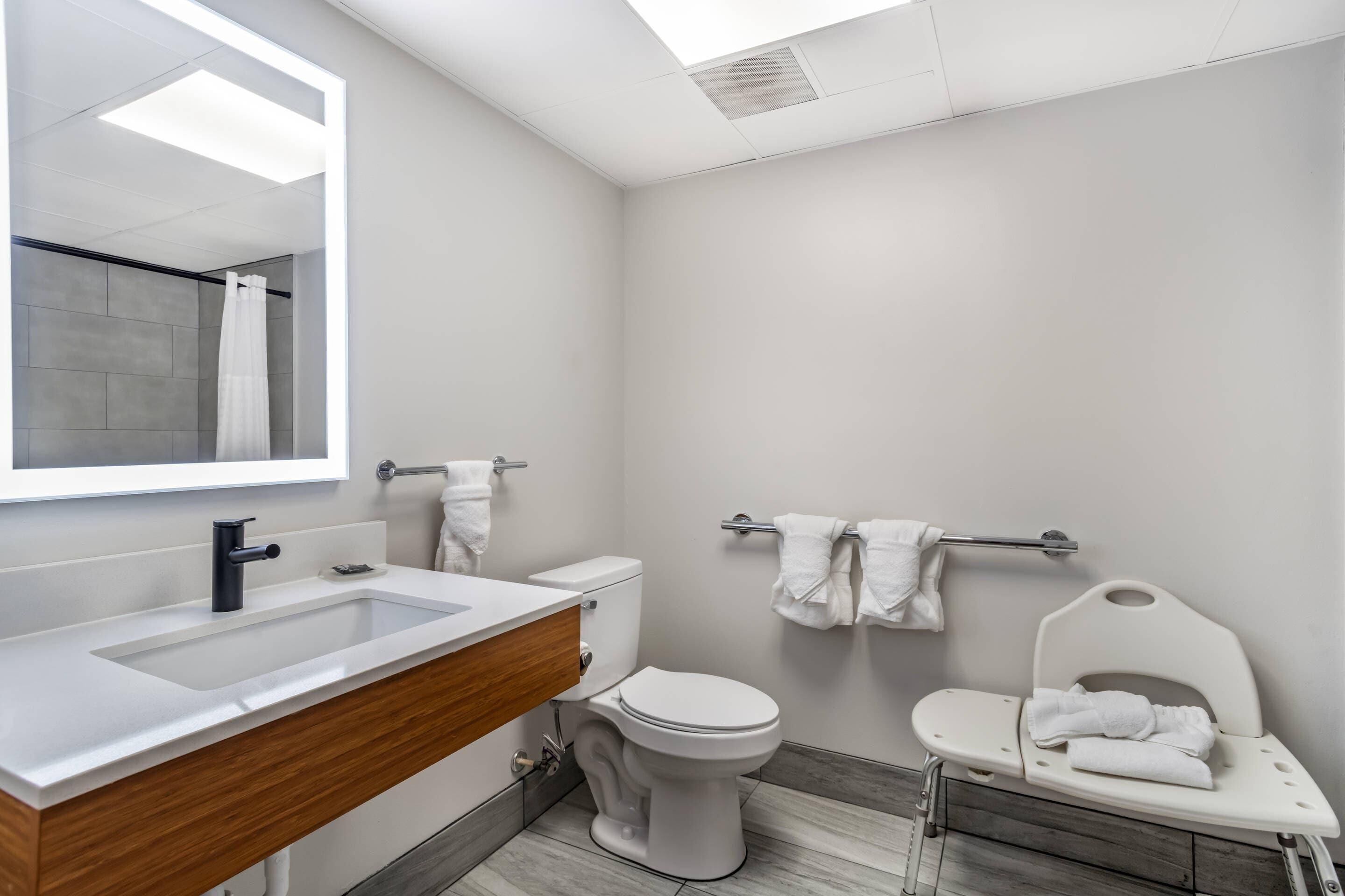 A modern bathroom with a large mirror, white sink, toilet, and a baby changing station.