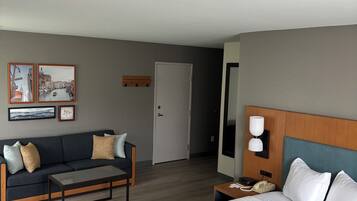 Habitación de hotel con cama, sofá, mesa de centro, mesita de noche con lámpara y una puerta.