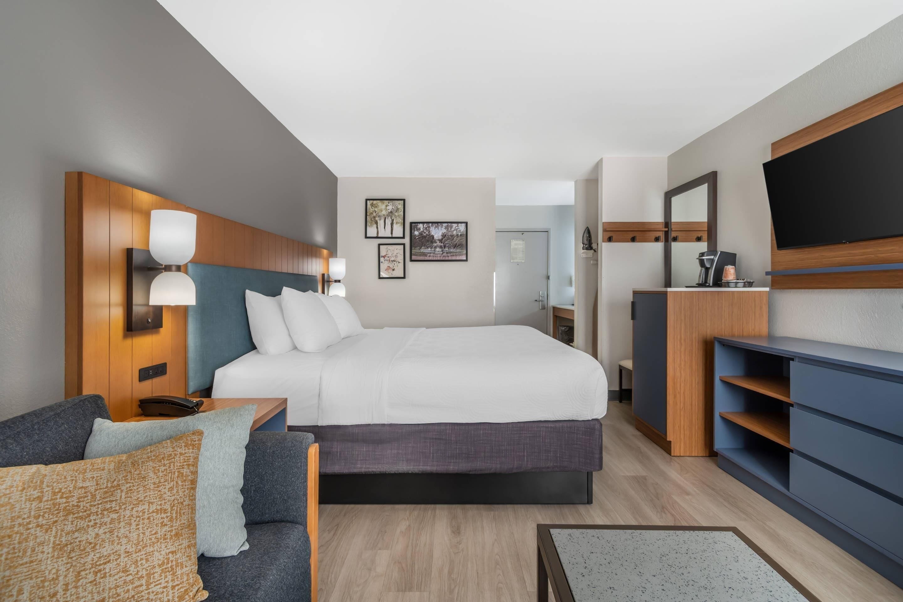 A modern hotel room with a large bed, a sofa, a desk, and a TV.