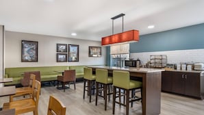 A modern kitchen with a bar area, wooden chairs, and a green sofa.