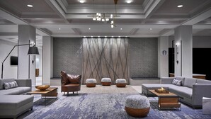 A modern hotel lobby with a sectional sofa, leather armchair, ottomans, and a patterned rug.