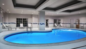 An indoor swimming pool with a tiled edge, surrounded by lounge chairs and a tiled wall with a blue and white pattern.