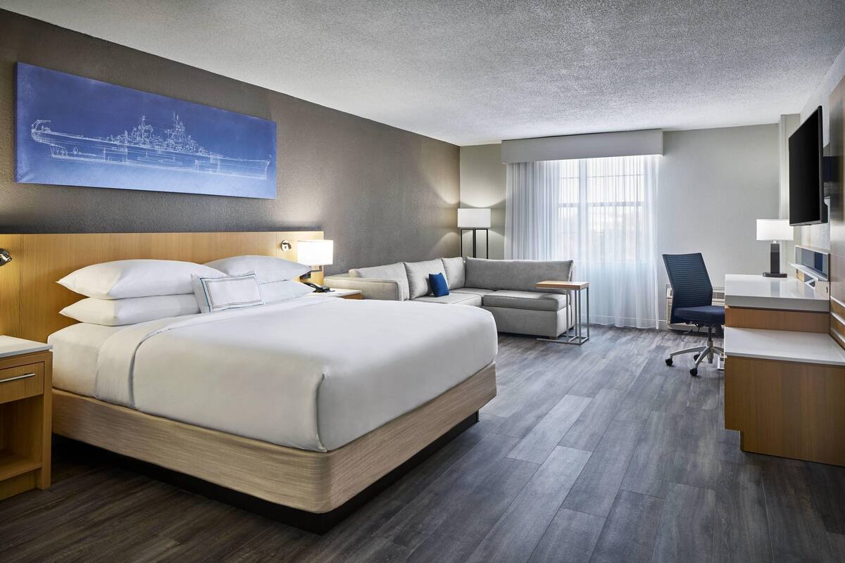 A modern hotel room with a large bed, a desk, a chair, and a television.
