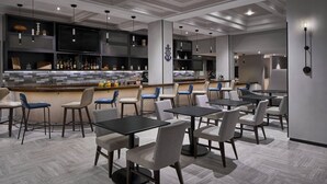 A modern restaurant with a bar area, multiple seating options including tables and chairs, and a decorative wall with a clock.