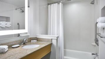 Un baño moderno con lavamanos de encimera de granito, un espejo grande, ducha con cortina y una bañera blanca.