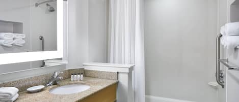 Un baño moderno con lavamanos de encimera de granito, un espejo grande, ducha con cortina y una bañera blanca.
