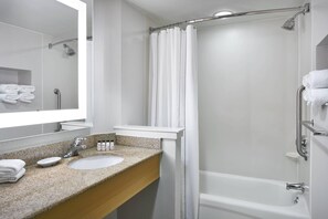 Un baño moderno con lavamanos de encimera de granito, un espejo grande, ducha con cortina y una bañera blanca.