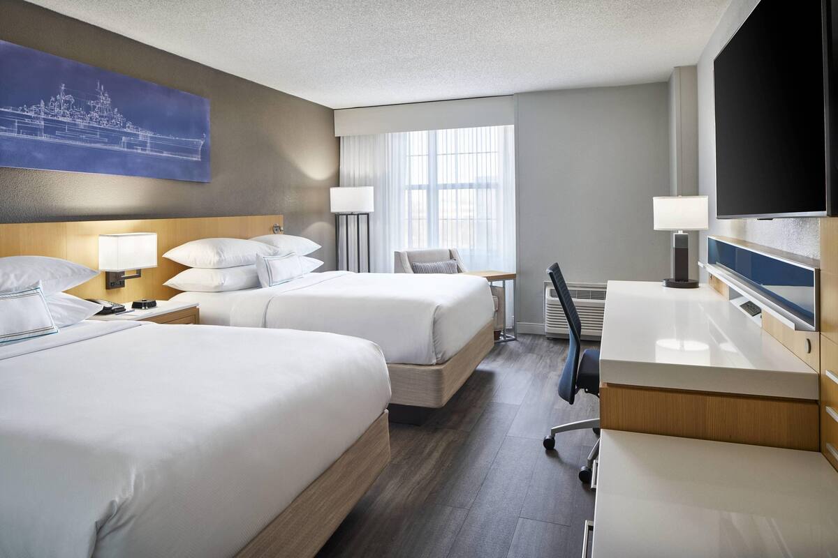 A hotel room with two beds, a desk, a chair, a TV, and a window with curtains.