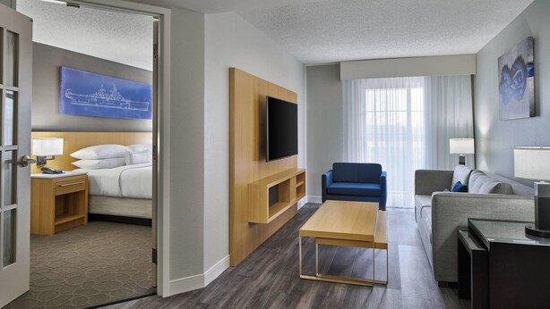 A hotel room with a bed, a TV, a wooden TV stand, a sofa, a coffee table, and a window with curtains.