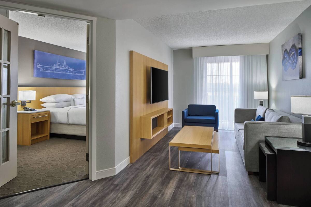 A hotel room with a bed, a TV, a wooden TV stand, a sofa, a coffee table, and a window with curtains.