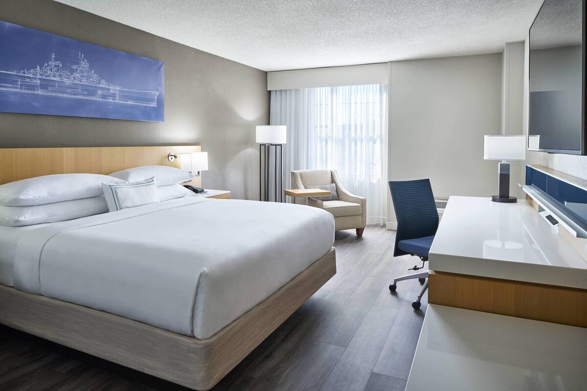 A hotel room with a large bed, a desk, a chair, a lamp, and a television.