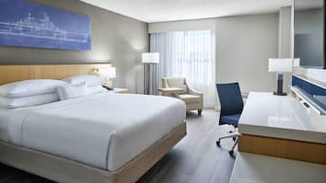 A hotel room with a large bed, a desk, a chair, a lamp, and a television.