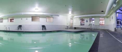 An indoor swimming pool with clear water, tiled walls, and a few chairs along the edge.
