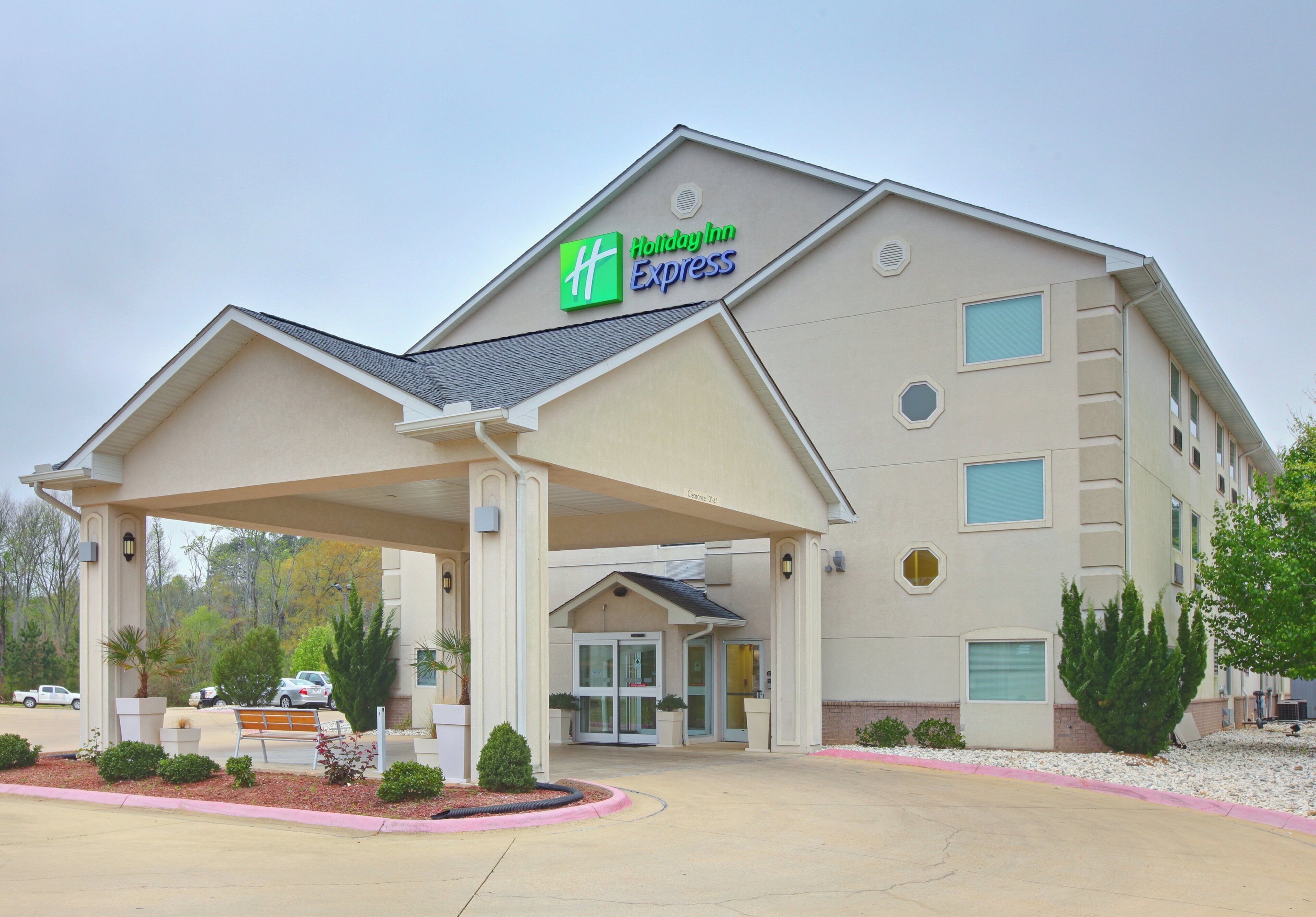A Holiday Inn Express building with a covered entrance, a parking lot, and a landscaped area with small shrubs.