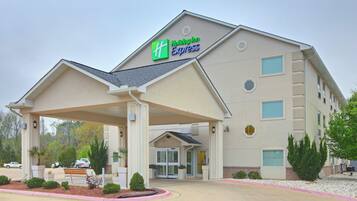 A Holiday Inn Express building with a covered entrance, a parking lot, and a landscaped area with small shrubs.
