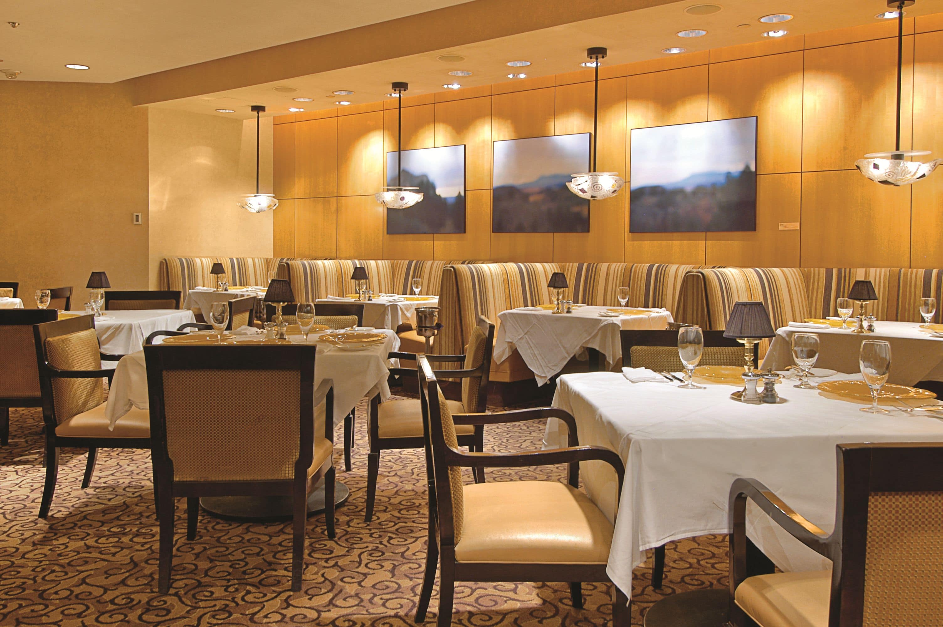 Un comedor con varias mesas y cabinas, cada una con manteles blancos y detalles dorados.