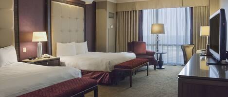 A hotel room with two beds, a desk with a television, and a chair.