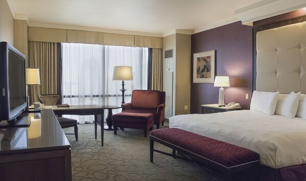 A hotel room with a bed, a desk, a chair, a television, and a lamp.