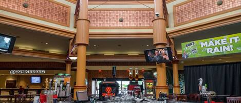 A bar area with multiple tables, a television screen, and a large promotional sign.