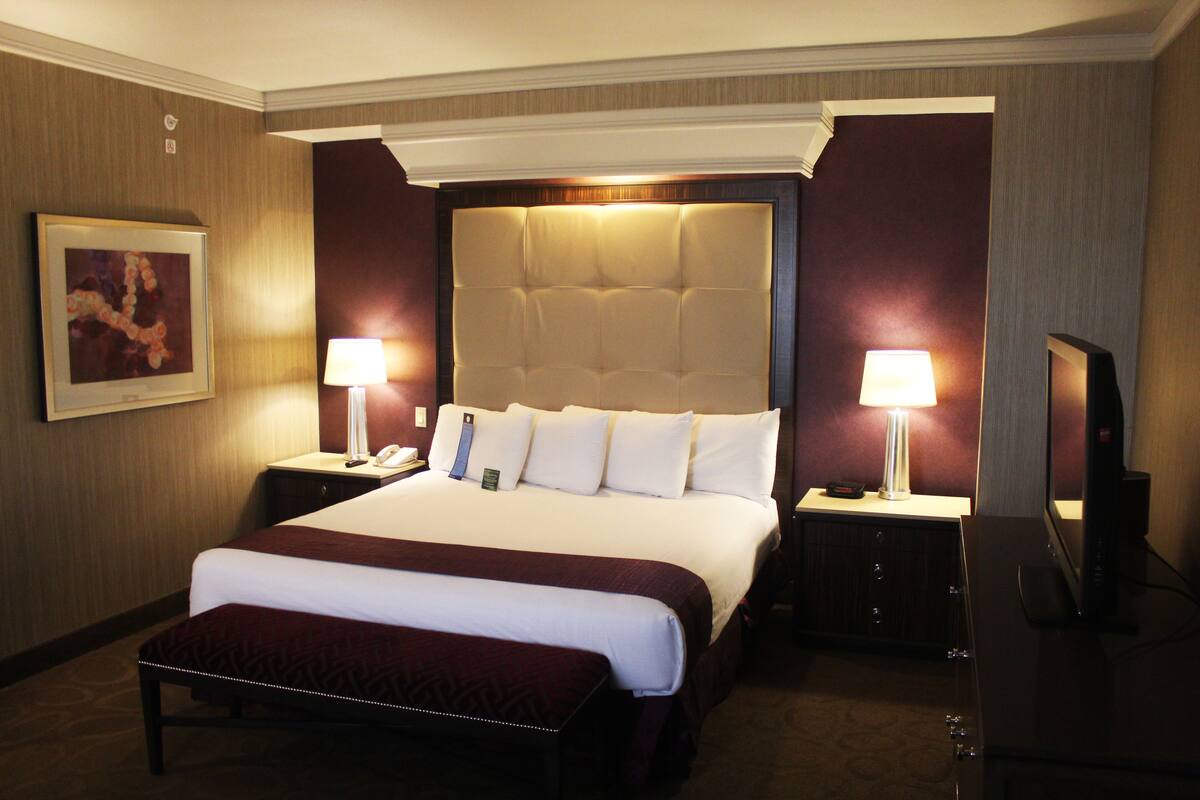 Habitación de hotel con una cama grande, dos mesitas de noche con lámparas, un televisor de pantalla plana y un cuadro en la pared.