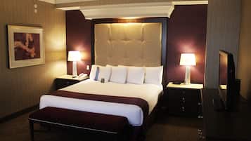 Quarto de hotel com uma cama grande, duas mesas de cabeceira com abajures, uma televisão de tela plana e um quadro na parede.