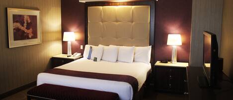 Una camera d'albergo con un letto grande, due comodini con lampade, una TV a schermo piatto e un quadro appeso alla parete.