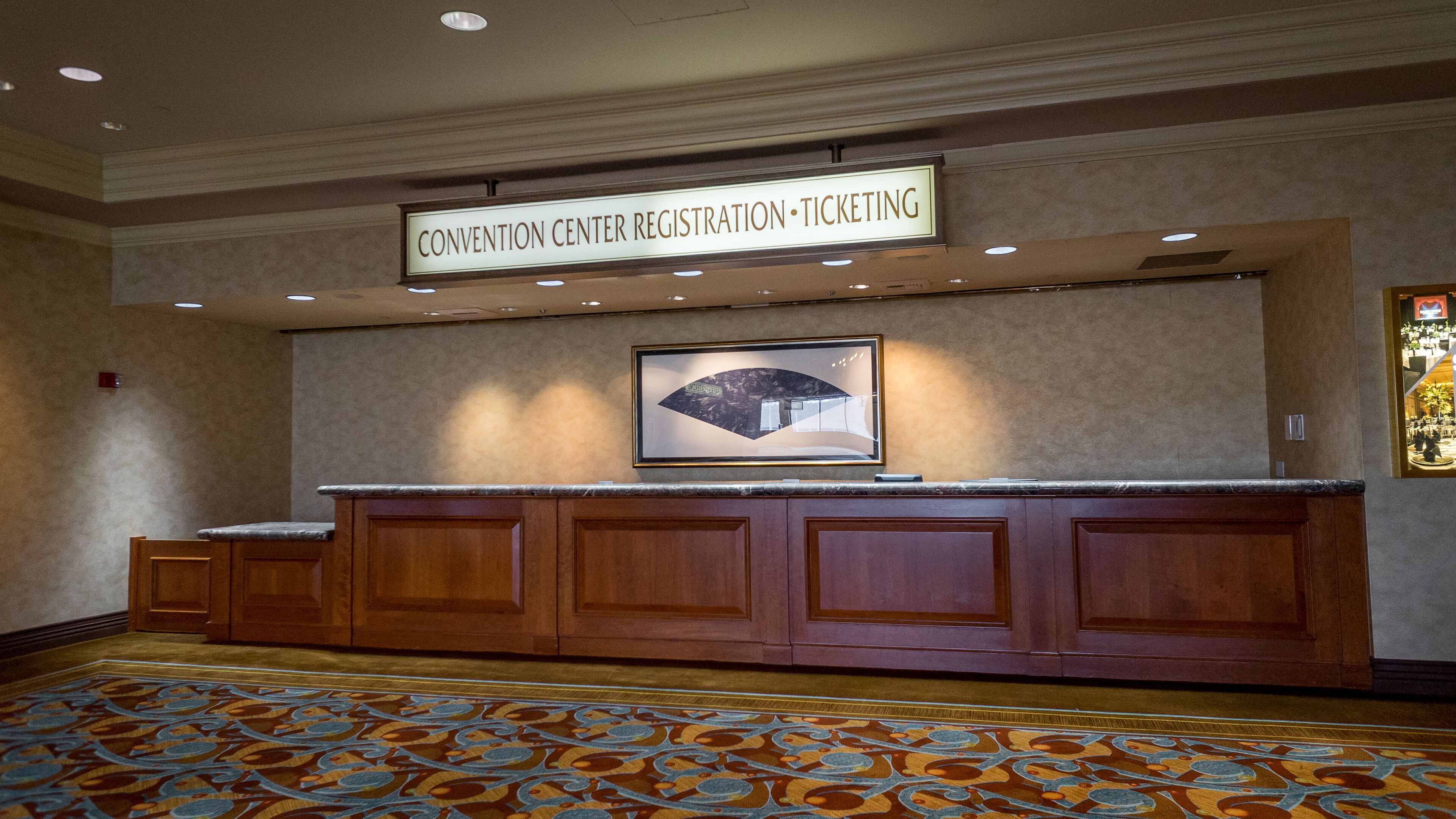 A convention center registration and ticketing area with a marble counter and patterned carpet.
