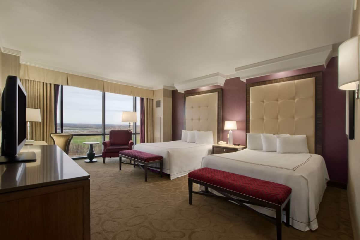 Habitación de hotel con dos camas, televisión, escritorio y vistas al exterior.