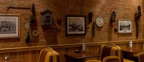 A restaurant with a brick wall and vintage decor, including framed pictures and a neon sign.