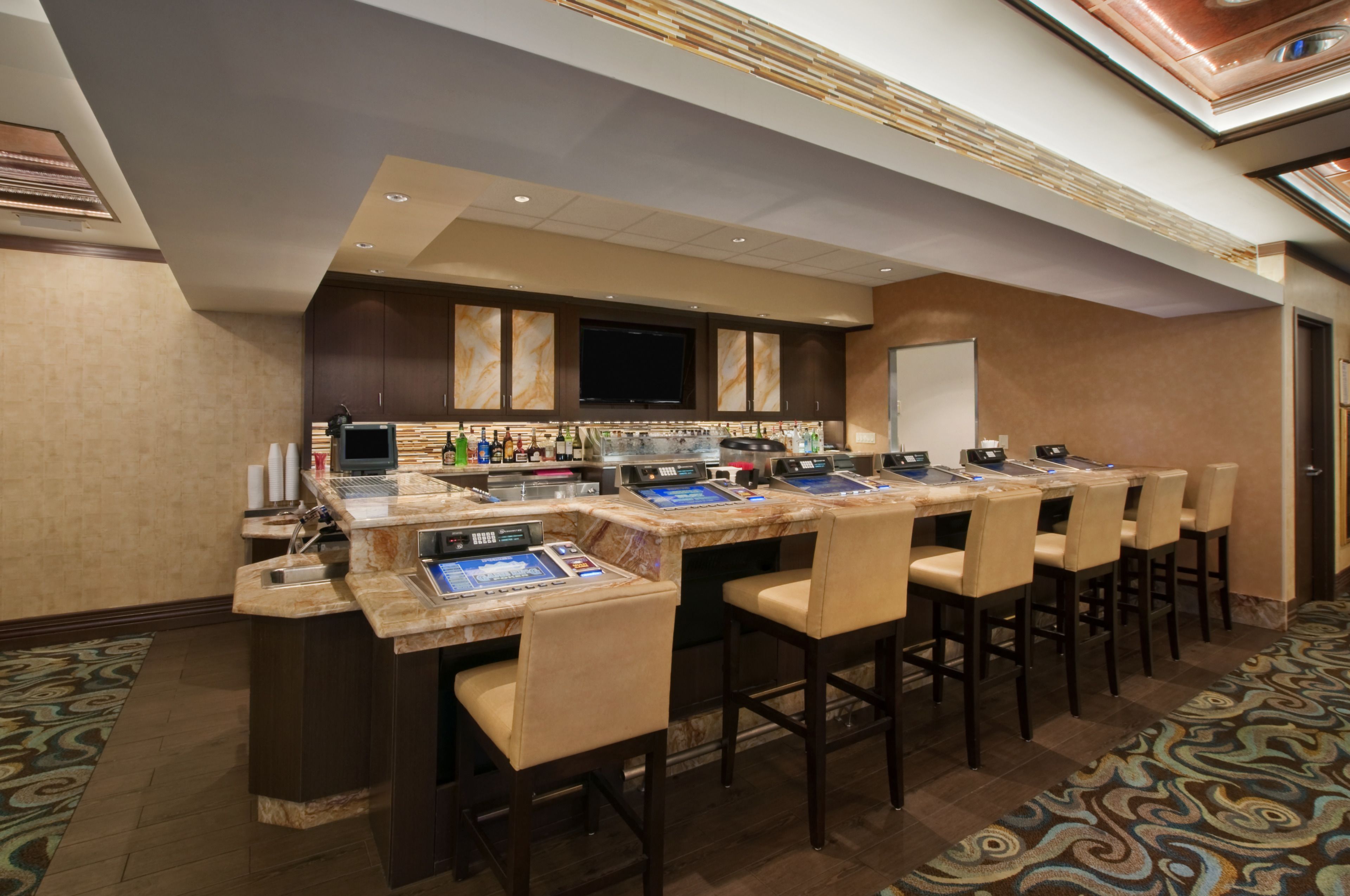 A bar area with multiple seating options, a television screen, and a variety of beverages.