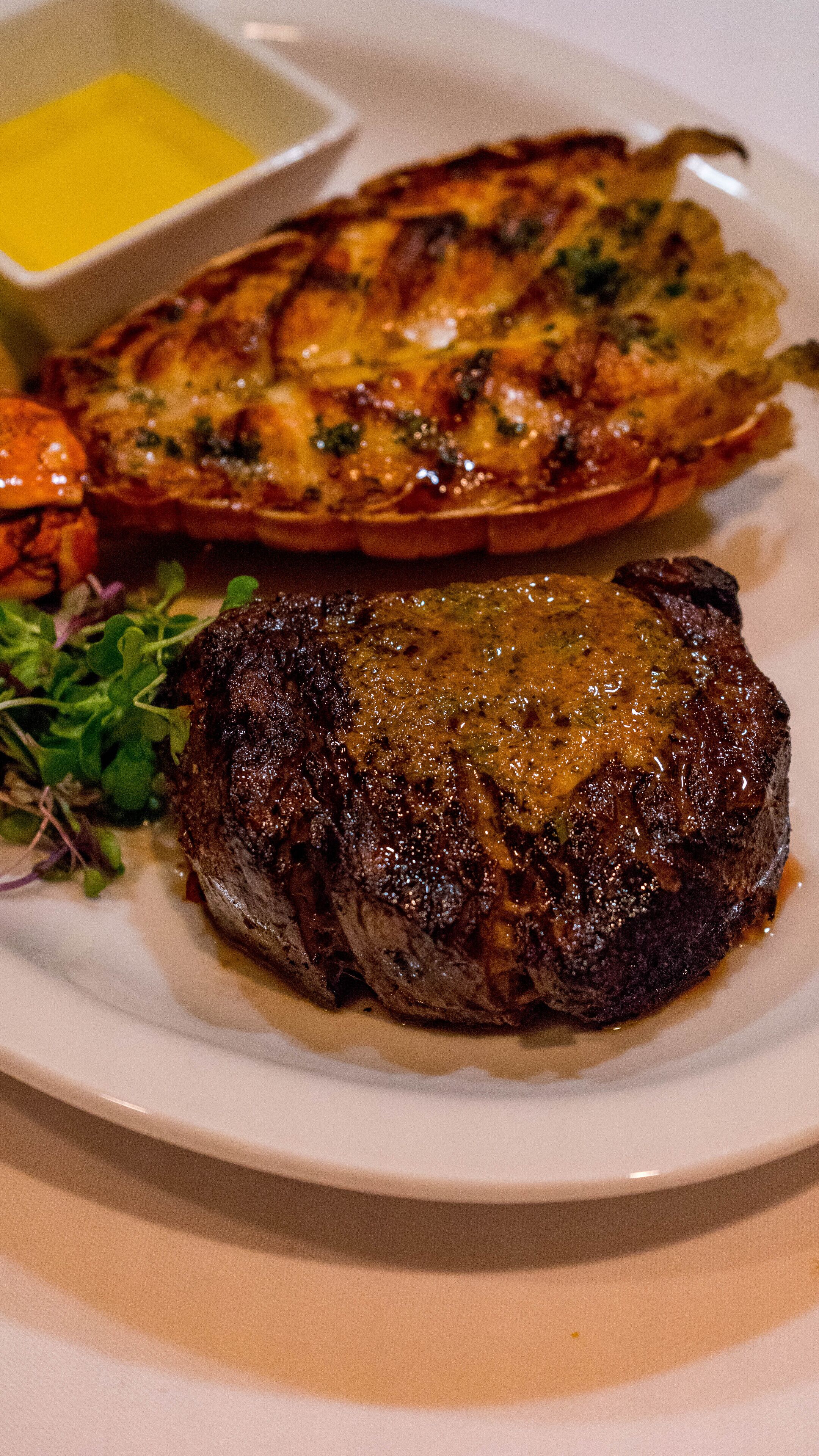 A plate with a steak and a baked dish, possibly a casserole, with a small bowl of sauce.